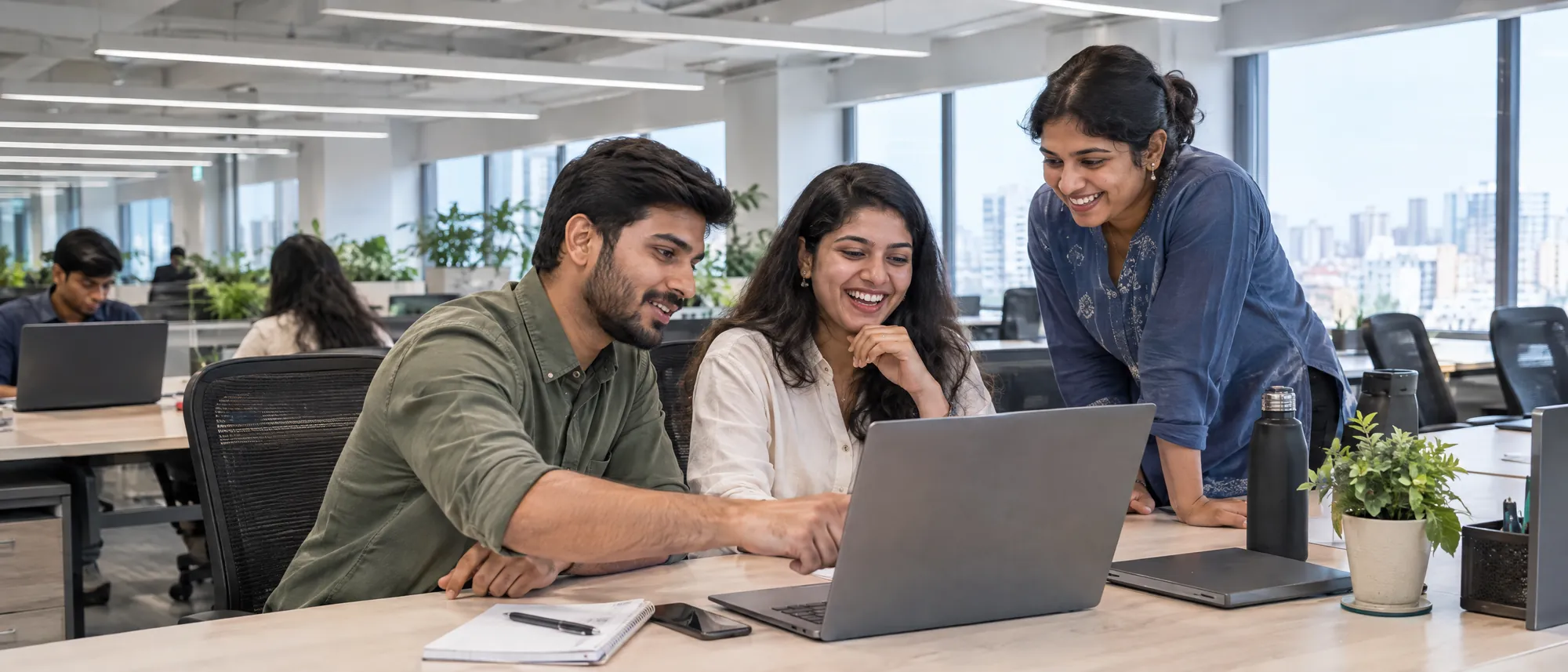 Colleagues laughing together at a shared desk in a bright open-plan office